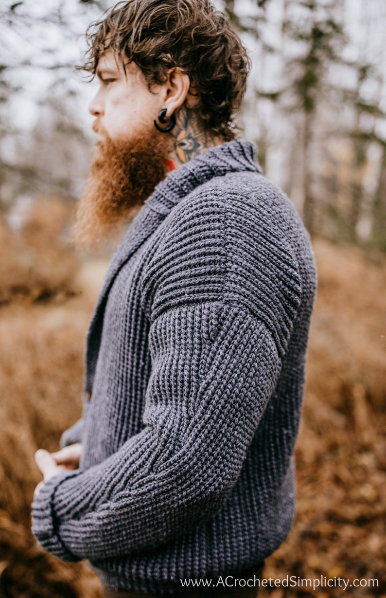 May include: A gray knitted cardigan with a textured stitch pattern. The cardigan has a collar and long sleeves. The cardigan is worn by a person with a beard and a tattoo on their neck.