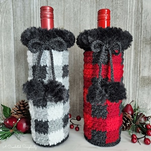 Puede incluir: Dos fundas para botellas de vino, una con un estampado de cuadros de búfalo en blanco, negro y gris y la otra en rojo y negro. Ambas tienen un ribete negro y esponjoso en la parte superior y pompones negros. Las botellas tienen tapones rojos.