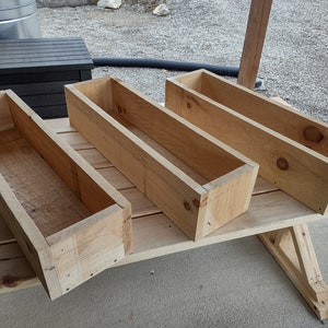 Puede incluir: Cuatro jardineras de madera sin terminar, hechas de madera natural, est&aacute;n apiladas unas sobre otras en una superficie de madera.