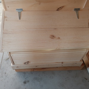 May include: A wooden storage box with a hinged lid and two metal hinges. The box is made of unfinished wood and has a simple design.