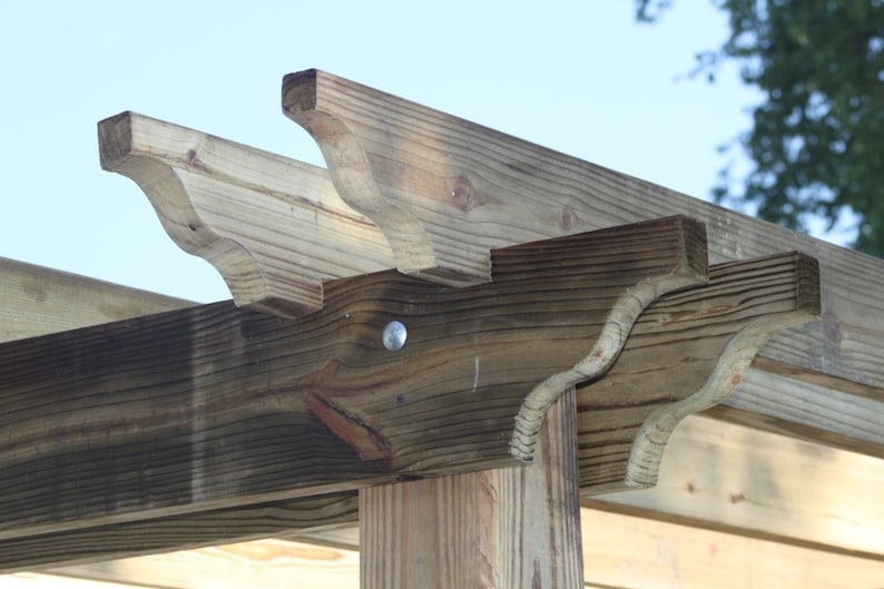 May include: A wooden pergola with a decorative, curved design on the top beams. The pergola is made of natural wood with a weathered finish.