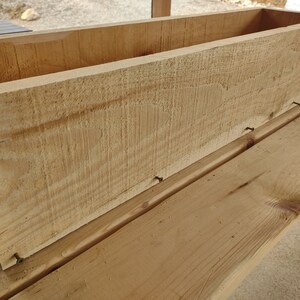Puede incluir: Una caja de madera para plantar con un acabado natural. La caja se est&aacute; ensamblando con clavos. La caja est&aacute; sentada sobre una superficie de madera.