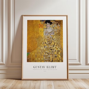 Puede incluir: Una impresión artística enmarcada del Retrato de Adele Bloch-Bauer de Gustav Klimt. La obra muestra a una mujer con un vestido dorado estampado sobre un fondo dorado brillante. El texto GUSTAV KLIMT PORTRAIT OF ADELE BLOCH-BAUER 1907 aparece impreso debajo.