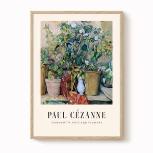 Op de afbeelding: Een ingelijste prent van een stilleven schilderij van Paul Cézanne. Het kunstwerk toont terracotta potten en bloemen, met een witte kan en een rood-oranje patroon doek. De prent heeft een lichtbeige achtergrond en is ingelijst in licht hout.