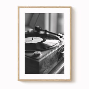 Puede incluir: Fotografía en blanco y negro de un tocadiscos vintage. El tocadiscos presenta un disco de vinilo con una etiqueta blanca. El mueble de madera tiene una perilla y otros controles. La imagen está enmarcada.