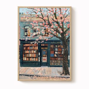 Op de afbeelding: Een ingelijste kunstdruk van een boekhandelfaçade met de tekst "BOOK BROS" en "NEWER" boven de ingang. Een grote boom met roze bloesems omlijst het gebouw. De boekhandel heeft veel boeken tentoongesteld. Het gebouw is geschilderd in blauw- en bruintinten.