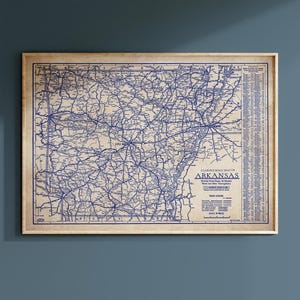 May include: A vintage-style Clason's Road Map of Arkansas printed in dark blue ink on a tan background. The map displays detailed road networks, a road legend, and a list of cities and towns. It is framed in a light-colored wooden frame.