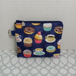 May include: A small blue zippered pouch with a donut, cupcake, and coffee cup pattern. The pouch has a silver zipper pull with a small cupcake charm.