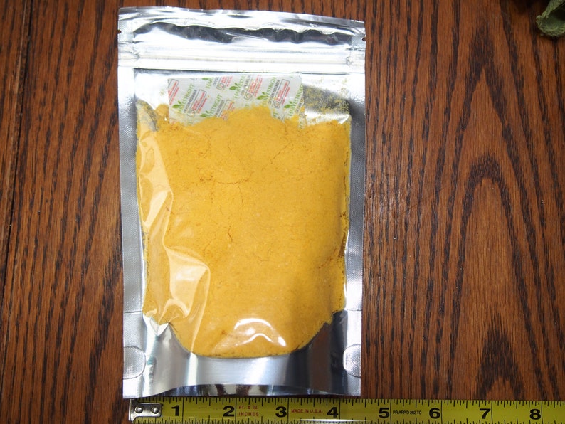 May include: A silver resealable pouch filled with a bright yellow powder. The pouch is sitting on a wooden surface.