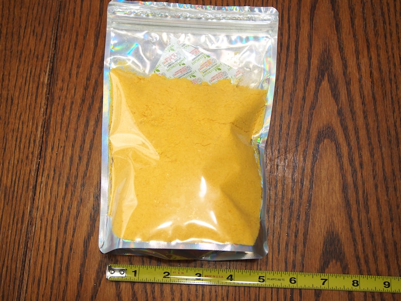 May include: A clear plastic bag with a silver iridescent finish contains a yellow powder. The bag is sealed with a zipper.