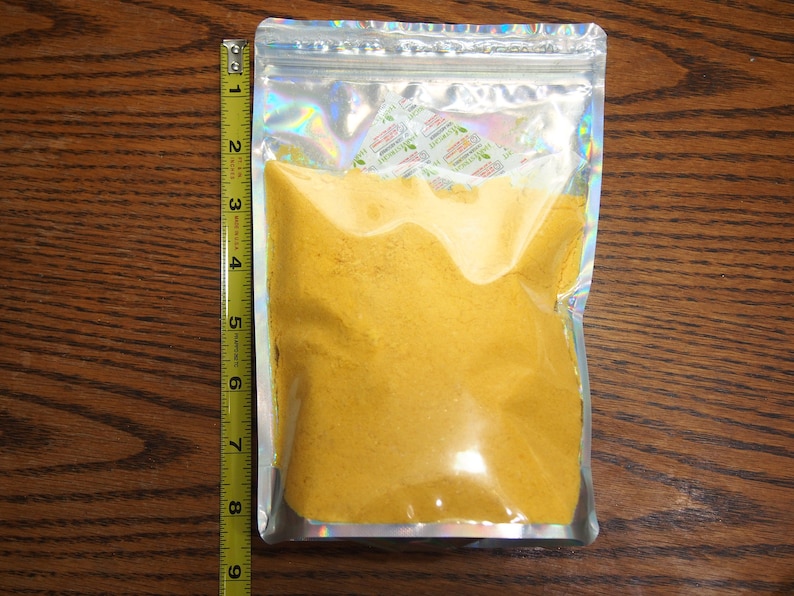 May include: A clear plastic bag with a silver iridescent finish contains a yellow powder. The bag is sealed with a zipper.