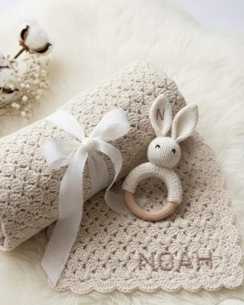 Personalized baby blanket in mushroom beige featuring the name 'NOAH' in a Handcrafted backstitch embroidery style. A cozy, neutral-toned nursery essantial shoen as a high-quality conceptual model.