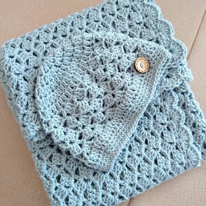 May include: A light blue crocheted blanket and matching pillow cover. The blanket features a detailed openwork pattern and a scalloped edge. The pillow cover is secured with a wooden button. The items are handmade and suitable for home decor.