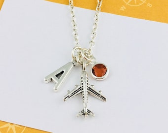 May include: Silver necklace with a silver airplane charm, a silver letter A charm, and a brown gemstone charm.