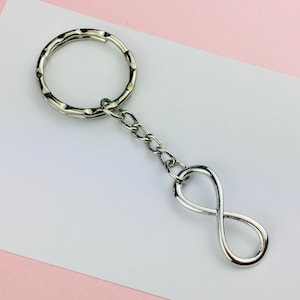 Op de afbeelding: Zilveren sleutelhanger met een oneindigheidssymbool, een sleutelring en een ketting.