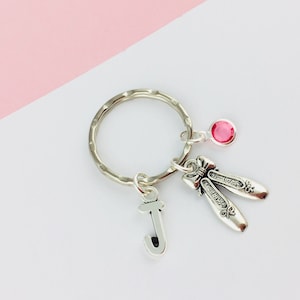 May include: Silver keyring with a pink rhinestone, a silver letter J charm, and a pair of silver ballet shoe charms.