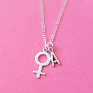 May include: A silver necklace with a charm of the female symbol and the letter A.