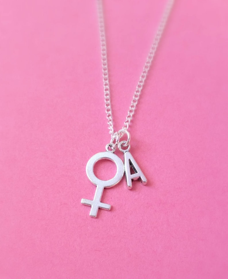 May include: A silver necklace with a charm of the female symbol and the letter A.