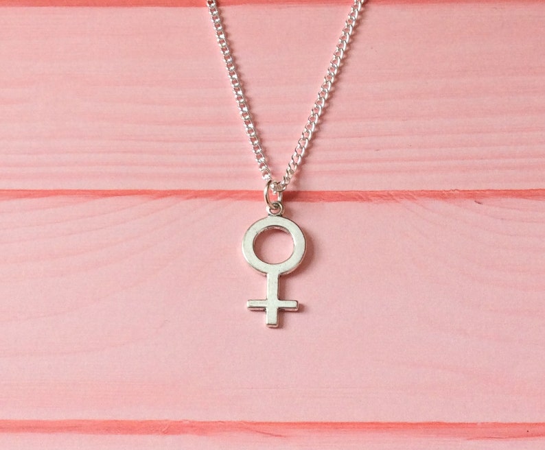 Puede incluir: Un collar de plata con un colgante simple y femenino en forma de s&iacute;mbolo femenino.