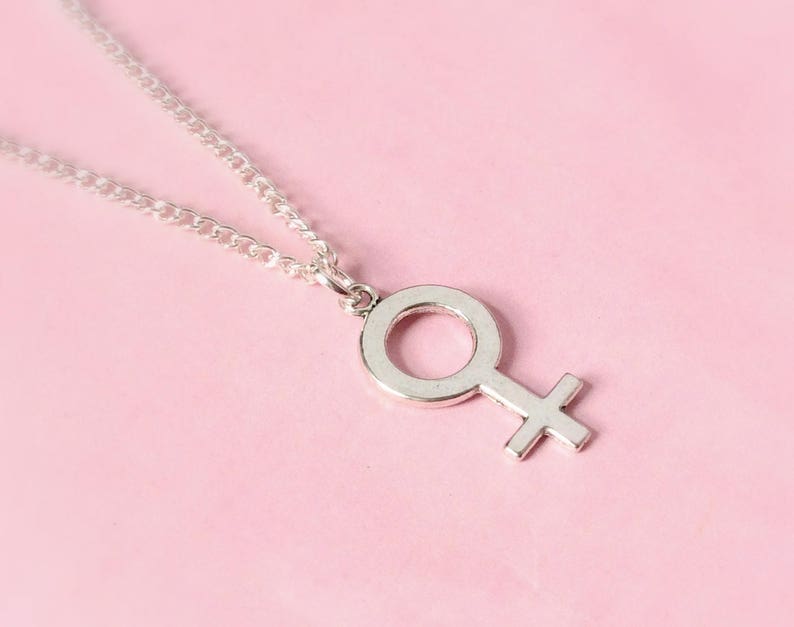 Puede incluir: Un collar de cadena de plata con un colgante de plata en forma de s&iacute;mbolo femenino.