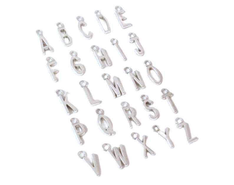 May include: A collection of twenty-six individual silver-toned metal alphabet letter charms, each featuring a small circular loop at the top for attachment. The letters are arranged in a loose grid pattern, representing the complete English alphabet from A to Z.