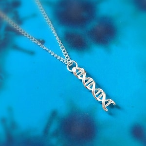Op de afbeelding: Een zilveren ketting met een DNA-dubbele helix hanger. De ketting ligt op een blauwe achtergrond.
