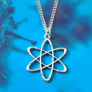 May include: A silver atom pendant necklace. The pendant has a stylized atom design with orbiting electrons. The necklace hangs on a delicate chain against a blue background.