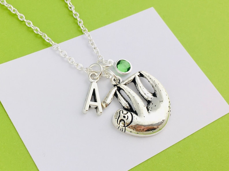 May include: Silver necklace with a sloth charm, a letter 'A' charm, and a green gemstone.