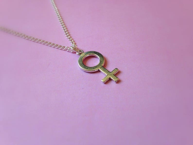 Puede incluir: Un collar de plata con un colgante de plata en forma de s&iacute;mbolo femenino.