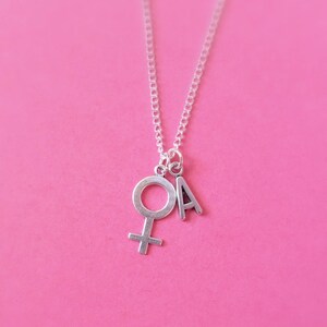 May include: A silver necklace with a charm of the female symbol and the letter A.