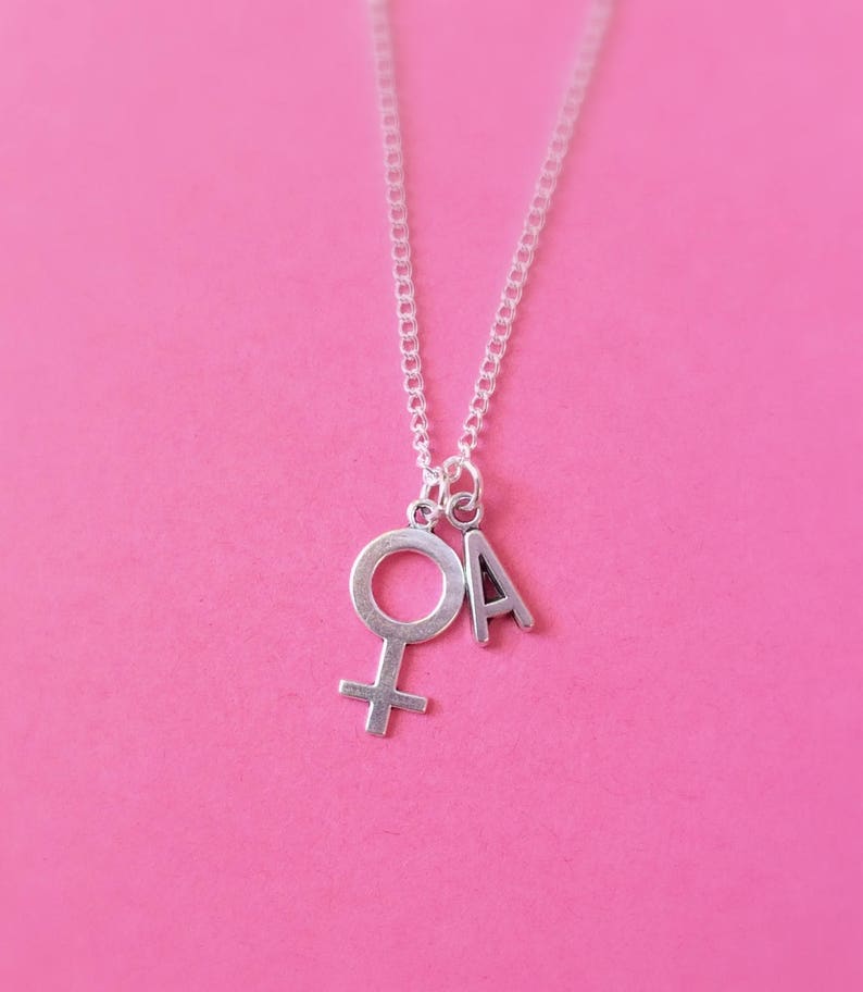 May include: A silver necklace with a charm of the female symbol and the letter A.