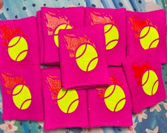 May include: A collection of pink terry cloth wristbands, each featuring a yellow tennis ball graphic with a red flame design. These wristbands are designed for sports and fitness activities.