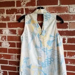 May include: A sleeveless, light blue and white patterned shirt with a keyhole back opening. The shirt has a button-up front and a collar.