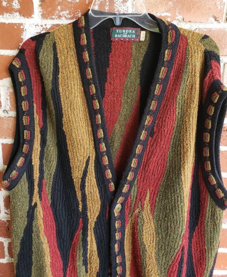 Puede incluir: Un su&eacute;ter sin mangas con un dise&ntilde;o colorido y texturizado. El su&eacute;ter presenta rayas verticales en negro, rojo, verde oliva y dorado. El cuello y los bordes est&aacute;n adornados con un color oscuro y costuras decorativas. La etiqueta dice "Tundra Bachrach."