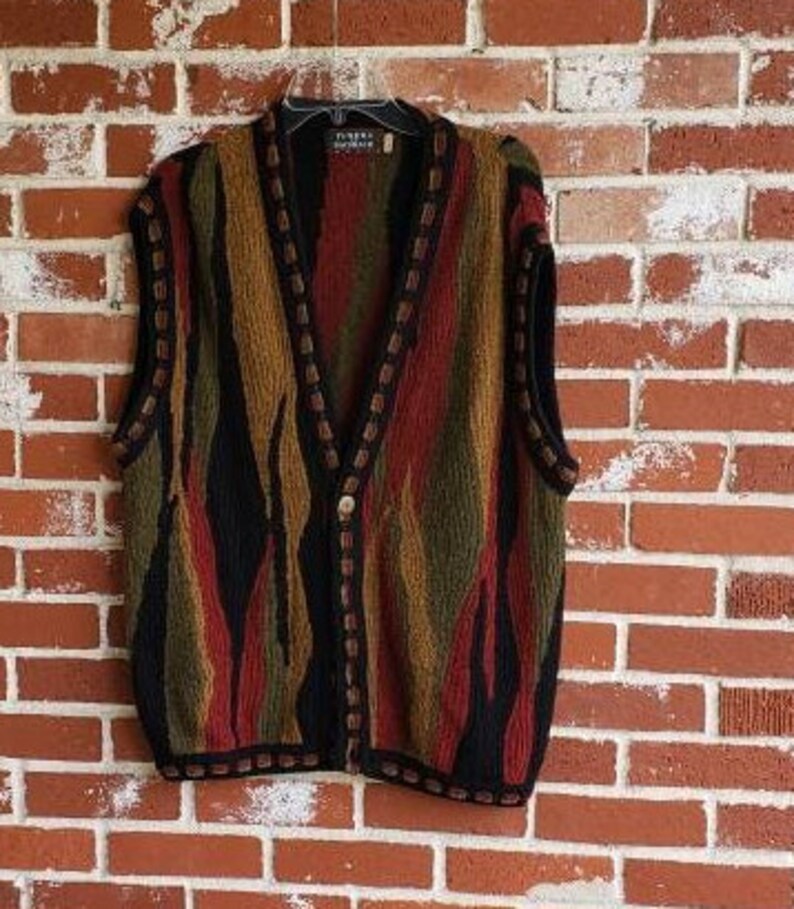 Puede incluir: Un chaleco multicolor con botones y cuello en V. El chaleco presenta rayas verticales en tonos negro, marr&oacute;n, rojo y verde. Los bordes est&aacute;n ribeteados con un borde marr&oacute;n oscuro. El chaleco est&aacute; colgado de una percha negra.