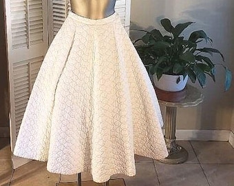 May include: A white quilted circle skirt with a gathered waistline. The skirt is full and flowing, and it is made of a soft, lightweight fabric.