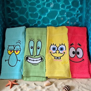 May include: Four colorful bath towels featuring embroidered cartoon character faces. The towels are light blue, green, yellow, and red. A starfish, a seashell, and a striped snail shell are in the foreground.