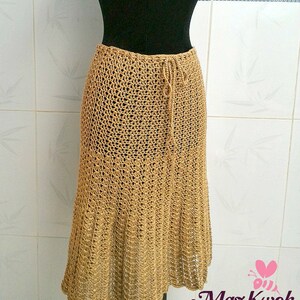 May include: A long, brown crocheted skirt with a drawstring waist. The skirt is made of a delicate, open-weave fabric and has a flowing, A-line silhouette.