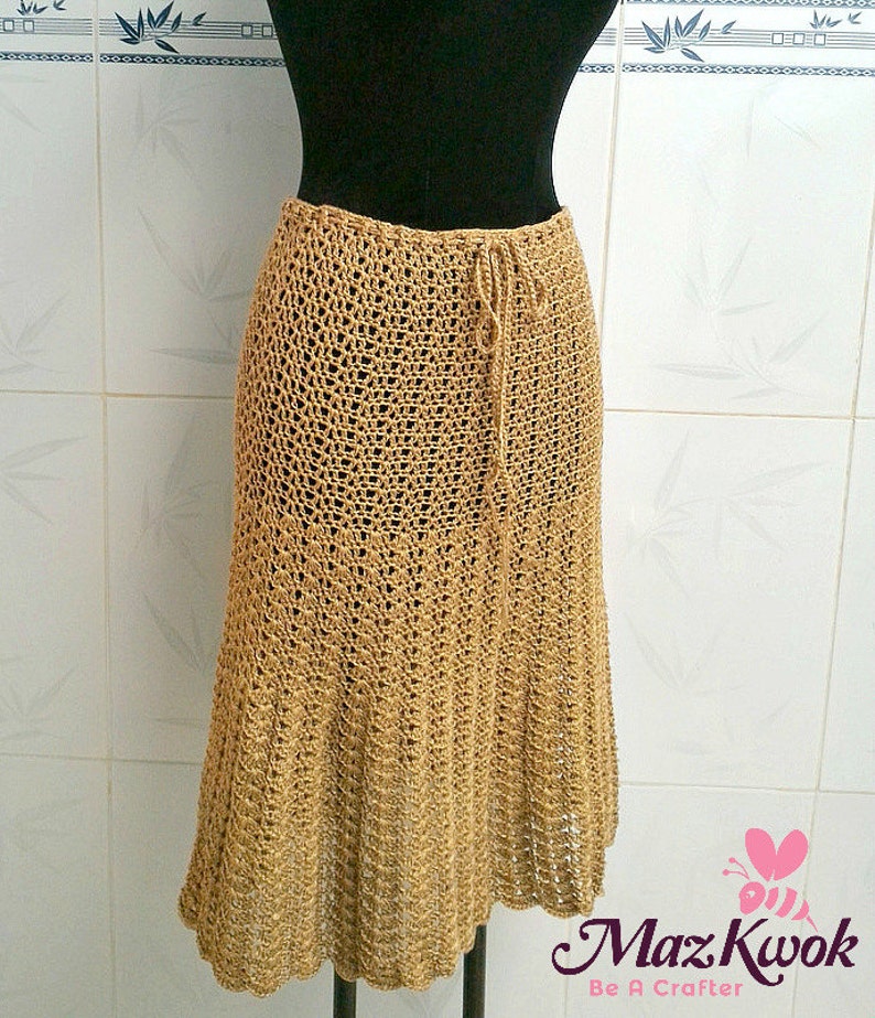 May include: A long, brown crocheted skirt with a drawstring waist. The skirt is made of a delicate, open-weave fabric and has a flowing, A-line silhouette.
