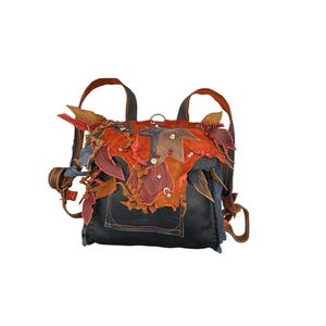 May include: A unique, handmade backpack with a black base and decorative accents. The backpack features a patchwork design with orange, red, and brown leaf-shaped embellishments. It has adjustable straps and a small front pocket.