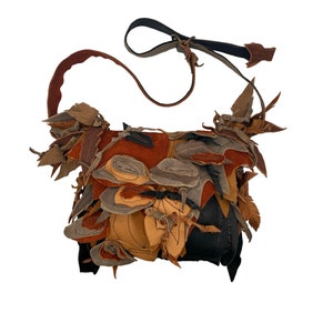 May include: A small, brown leather crossbody bag with a unique, patchwork design. The bag is made of various pieces of leather sewn together, creating a textured and layered look. The bag has a long, adjustable strap.