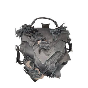Könnte beinhalten: Eine graue Ledertasche mit einem einzigartigen Design aus mehreren Lederschichten und floralen Verzierungen.