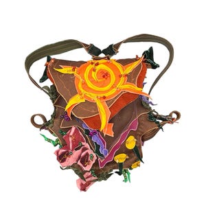 May include: A brown leather backpack with colorful fabric appliques, including a sun with a yellow spiral, pink flowers, and green beads.