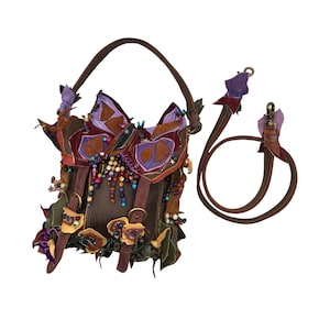 May include: A handcrafted brown leather handbag with a butterfly-shaped flap, decorated with purple, orange, and green fabric accents. The bag has a brown handle and a detachable shoulder strap, embellished with beads and floral details.
