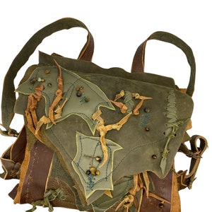 May include: A green leather backpack with brown leather straps and decorative stitching. The bag has a unique design with multiple layers of leather and beaded accents.