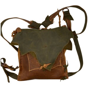 May include: A brown leather backpack with a green leather flap. The backpack has a unique design with stitching and decorative elements.