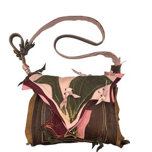 May include: A handcrafted shoulder bag with a unique patchwork design. The bag features a mix of brown, green, and pink leather pieces, with decorative stitching and small bow accents. The adjustable strap is a light brown color.