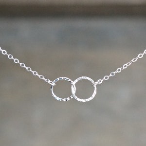 May include: A silver necklace with two interlocking circles. The circles are textured and have a hammered finish.