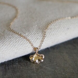 May include: A delicate gold-colored necklace featuring a small, detailed ginkgo leaf pendant. The pendant is intricately designed, showcasing the leaf's veining. The necklace chain is fine and elegant, creating a minimalist and nature-inspired aesthetic.
