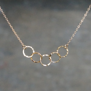 May include: A gold necklace with a chain and five connected, textured, circular pendants.